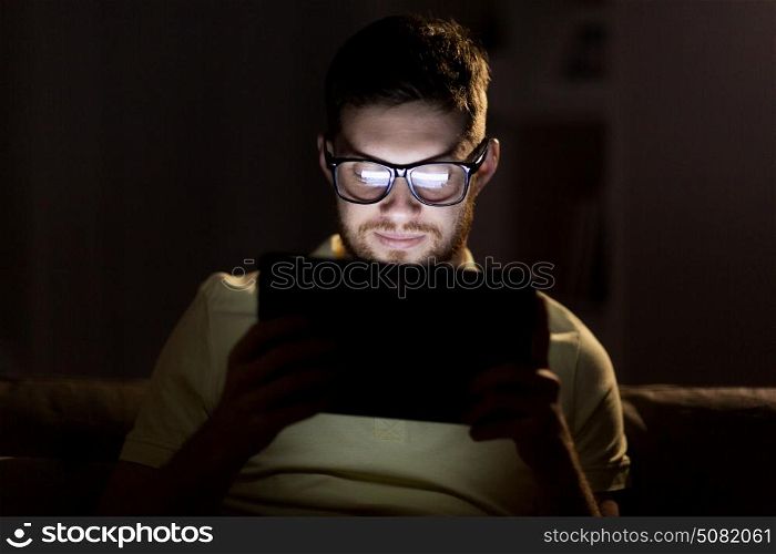 technology, internet, communication and people concept - young man in glasses with tablet pc computer networking at night at home. young man with tablet pc networking at night