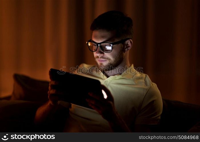 technology, internet, communication and people concept - young man in glasses with tablet pc computer networking at night at home. young man with tablet pc networking at night. young man with tablet pc networking at night