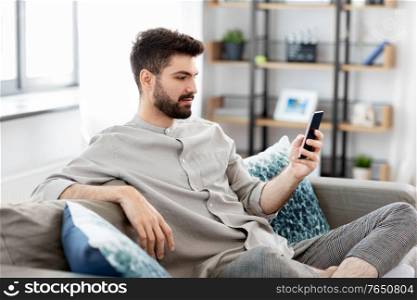 technology, internet, communication and people concept - young man texting on smartphone at home. young man with smartphone at home