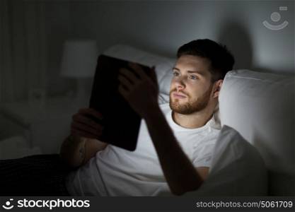 technology, internet, communication and people concept - young man with tablet pc computer in bed at home bedroom at night. young man with tablet pc in bed at home bedroom