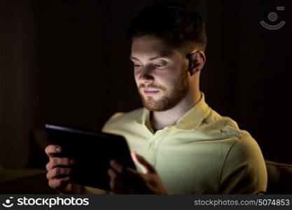 technology, internet, communication and people concept - young man with tablet pc computer at night at home. young man with tablet pc computer at night