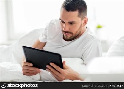 technology, internet, communication and people concept - young man with tablet pc computer in bed at home bedroom. young man with tablet pc in bed at home bedroom