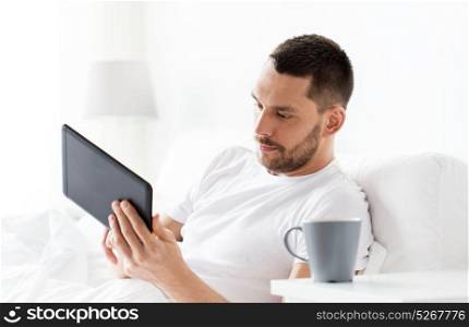 technology, internet, communication and people concept - young man with tablet pc computer in bed at home bedroom. young man with tablet pc in bed at home bedroom