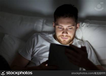 technology, internet, communication and people concept - young man with tablet pc computer in bed at home bedroom at night. young man with tablet pc in bed at home bedroom