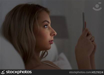 technology, internet, communication and people concept - young woman texting on smartphone in bed at home bedroom at night