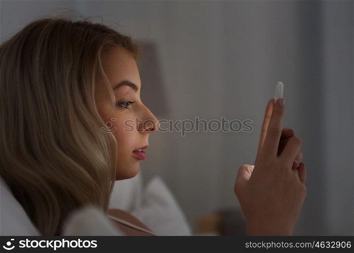 technology, internet, communication and people concept - young woman texting on smartphone in bed at home bedroom at night