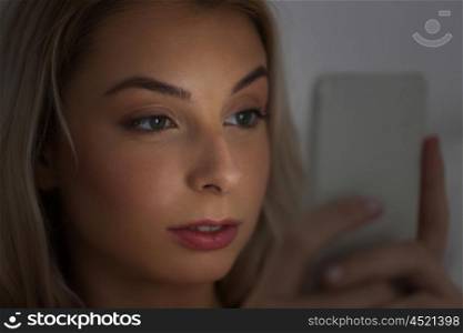 technology, internet, communication and people concept - young woman texting on smartphone at home at night