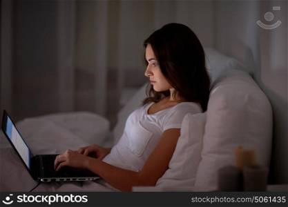 technology, internet, communication and people concept - young woman with laptop computer in bed at home bedroom at night. young woman with laptop in bed at home bedroom
