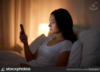 technology, internet, communication and people concept - young woman with smartphone in bed at home at night. young woman with smartphone in bed at night