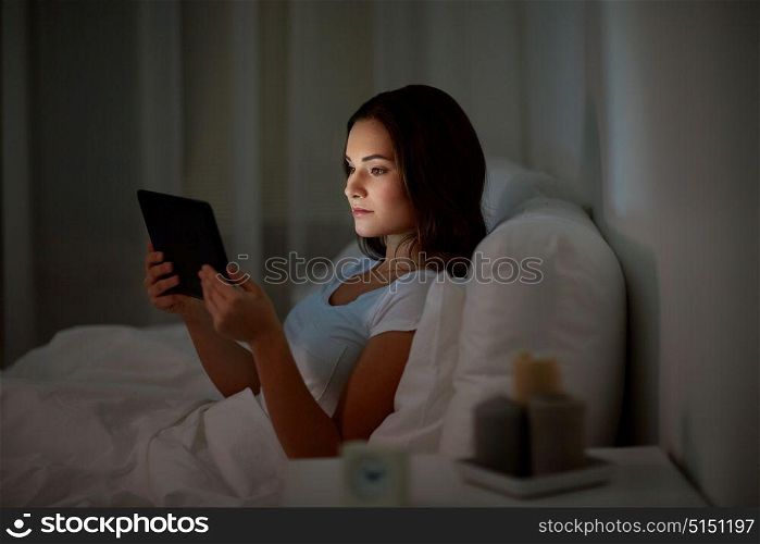 technology, internet, communication and people concept - young woman with tablet pc computer in bed at home bedroom at night. young woman with tablet pc in bed at home bedroom