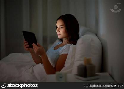 technology, internet, communication and people concept - young woman with tablet pc computer in bed at home bedroom at night. young woman with tablet pc in bed at home bedroom