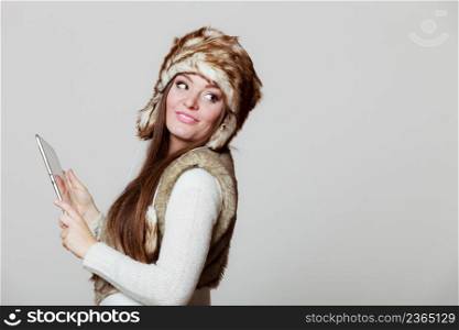 Technology internet concept. Happy fashion woman in winter clothes fur cap using digital tablet computer studio shot on gray