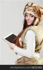 Technology internet concept. Happy fashion woman in winter clothes fur cap using digital tablet computer studio shot on gray