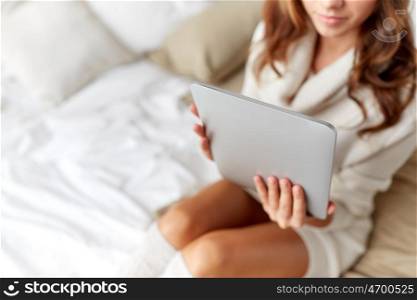 technology, internet, winter and people concept - young woman lying in bed with tablet pc computer at home bedroom