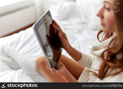 technology, internet, winter and people concept - young woman lying in bed with tablet pc computer at home bedroom
