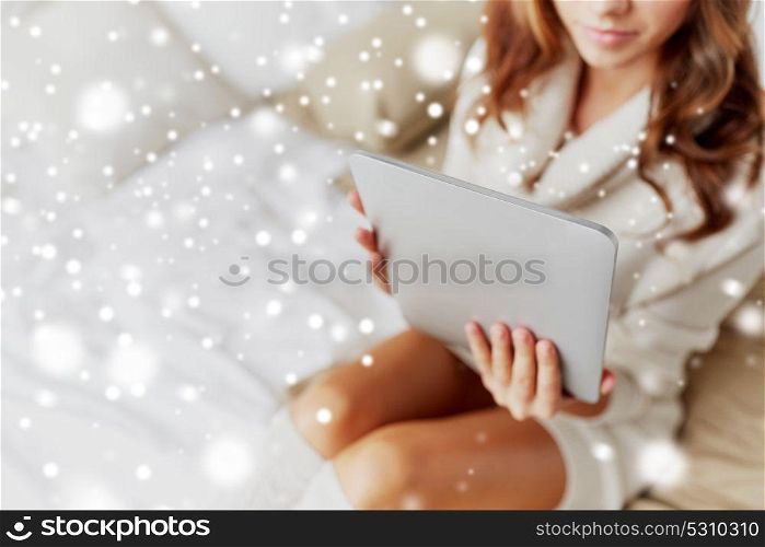 technology, internet, winter and people concept - young woman lying in bed with tablet pc computer at home over snow. young woman with tablet pc in bed at home