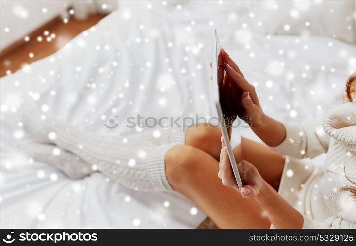 technology, internet, winter and people concept - young woman lying in bed with tablet pc computer at home over snow. young woman with tablet pc in bed at home