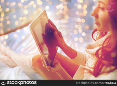 technology, internet, winter and people concept - young woman lying in bed with tablet pc computer at home bedroom. young woman with tablet pc in bed at home