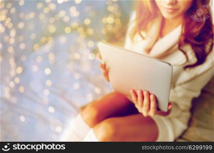 technology, internet, winter and people concept - young woman lying in bed with tablet pc computer at home bedroom. young woman with tablet pc in bed at home