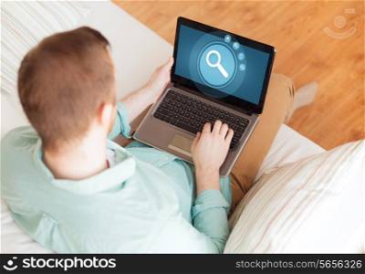 technology, leisure, advertisement and lifestyle concept - close up of man working with laptop computer displaying magnifying glass icon on screen and sitting on sofa at home