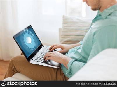 technology, leisure, advertisement and lifestyle concept - close up of man working with laptop computer displaying text bubble icon on screen and sitting on sofa at home