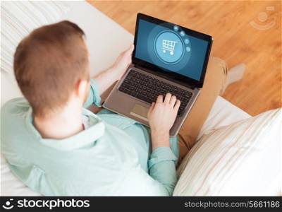 technology, leisure, advertisement and lifestyle concept - close up of man working with laptop computer displaying shopping trolley icon on screen and sitting on sofa at home