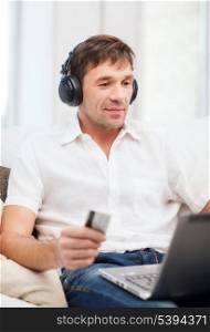 technology, leisure and lifestyle concept - happy man with headphones and credit card listening to music at home