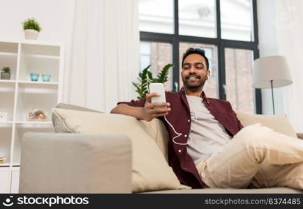 technology, leisure and people concept - happy man in earphones with smartphone listening to music at home. man in earphones listening to music on smartphone