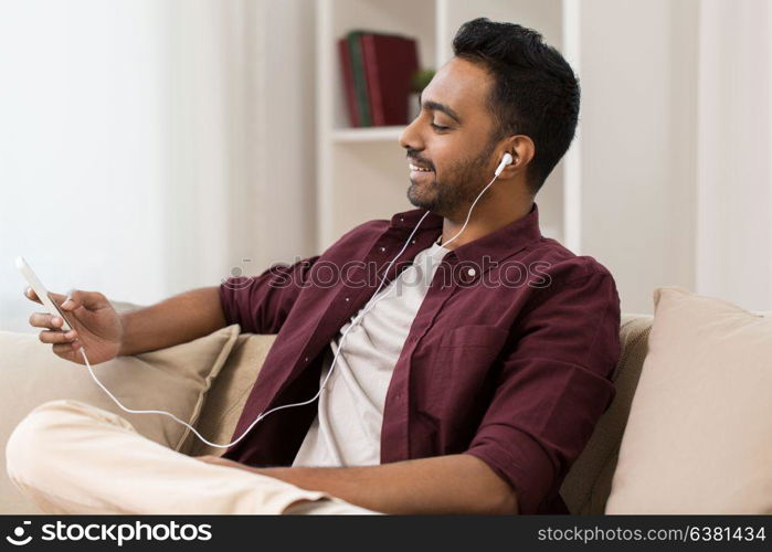 technology, leisure and people concept - happy man in earphones with smartphone listening to music at home. man in earphones listening to music on smartphone