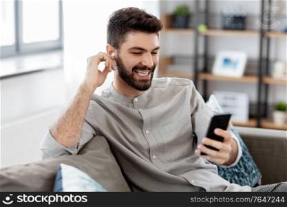 technology, leisure and people concept - happy man in earphones with smartphone listening to music at home. man in earphones listening to music on smartphone