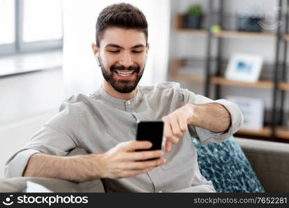 technology, leisure and people concept - happy man in earphones with smartphone listening to music at home. man in earphones listening to music on smartphone