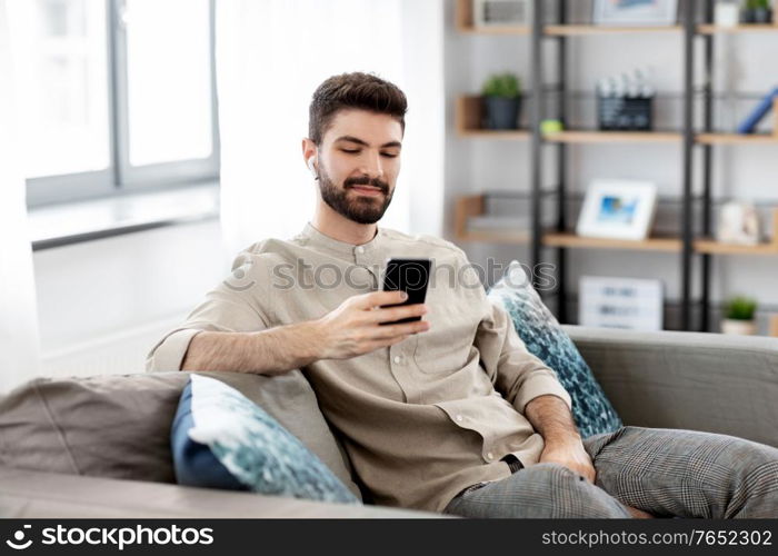 technology, leisure and people concept - happy man in earphones with smartphone listening to music at home. man in earphones listening to music on smartphone