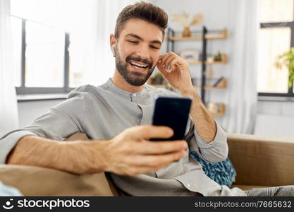 technology, leisure and people concept - happy man in earphones with smartphone listening to music at home. man in earphones listening to music on smartphone