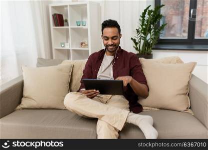 technology, leisure and people concept - happy man in earphones with tablet pc computer listening to music at home. man in earphones with tablet pc listening to music