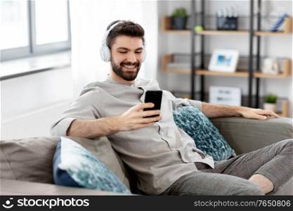 technology, leisure and people concept - happy man in headphones with smartphone listening to music at home. man in headphones listening to music on smartphone