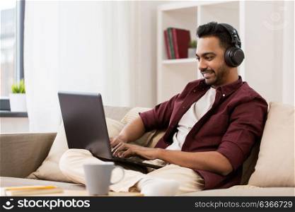 technology, leisure and people concept - happy man in wireless headphones with laptop computer listening to music at home. man in headphones with laptop listening to music