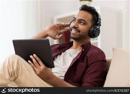 technology, leisure and people concept - happy man in wireless headphones with tablet pc computer listening to music at home. man in phones with tablet pc listening to music