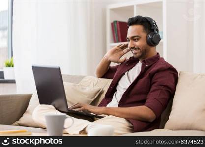 technology, leisure and people concept - happy man in wireless headphones with laptop computer listening to music at home. man in headphones with laptop listening to music