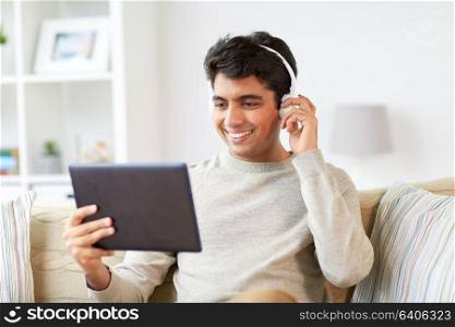 technology, leisure and people concept - happy man in wireless headphones with tablet pc computer listening to music at home. man in phones with tablet pc listening to music