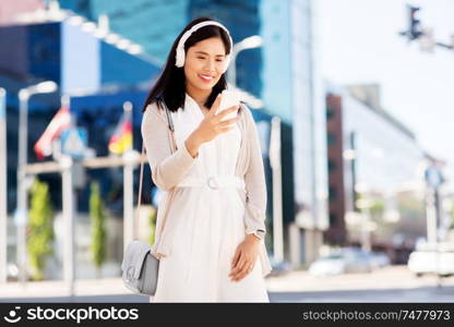 technology, leisure and people concept - happy smiling asian woman with smartphone and headphones listening to music in city. asian woman with smartphone and headphones in city