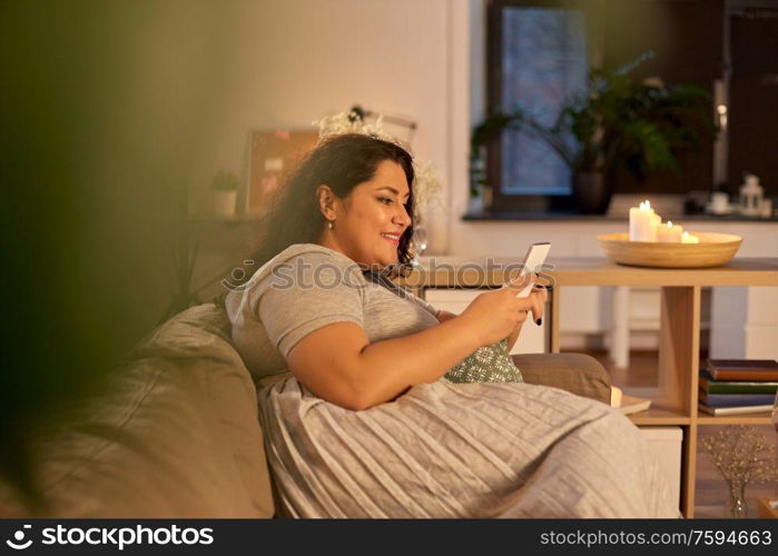 technology, leisure and people concept - happy smiling woman with smartphone at home in evening. woman with smartphone at home in evening