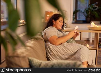 technology, leisure and people concept - happy smiling woman with smartphone at home in evening. woman with smartphone at home in evening