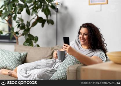 technology, leisure and people concept - happy smiling woman with smartphone drinking tea or coffee at home. woman with smartphone drinking coffee at home