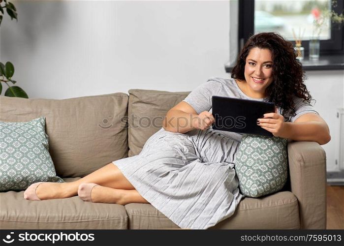 technology, leisure and people concept - happy smiling woman with tablet pc computer on sofa at home. woman with tablet pc computer on sofa at home