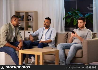 technology, leisure and people concept - man using smartphone and friends talking at home at night. man using smartphone while friends talking at home