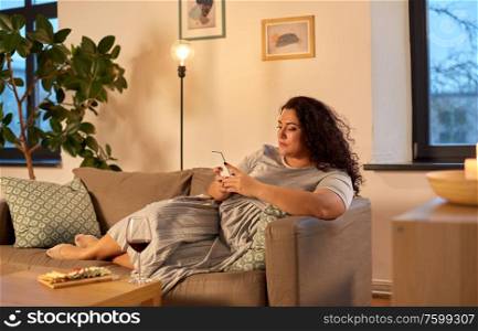 technology, leisure and people concept - woman with smartphone, red wine and snacks on table at home in evening. woman with smartphone at home in evening