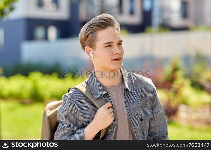 technology, leisure and people concept - young man or teenage boy with earphones and backpack walking in city. young man with earphones and backpack in city