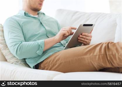 technology, leisure, lifestyle and distance learning concept - close up of man working with tablet pc computer sitting or lying on sofa at home