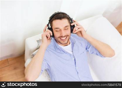 technology, leisure, people and happiness concept - smiling young man with closed eyes in headphones listening to music at home