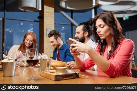 technology, lifestyle and people concept - bored woman dining with friends and messaging on smartphone at restaurant. bored woman messaging on smartphone at restaurant